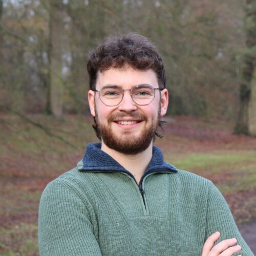 Foto van Thijmen Fellinger, met donker kort krullend haar en in een groene trui, met zijn armen over elkaar.